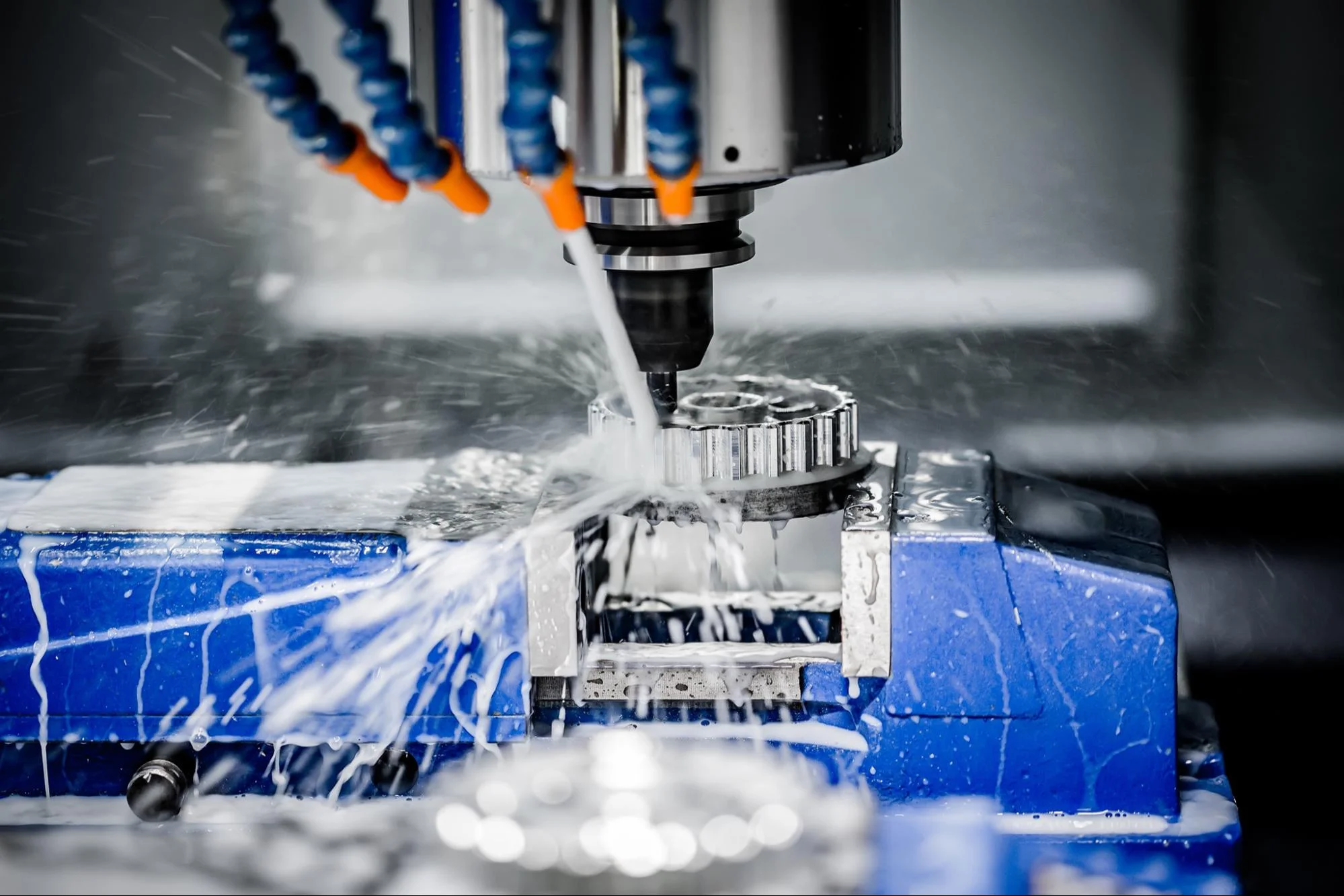 vise - Fictiv A metal hard being held in a vise in a CNC machine with coolant being sprayed on it