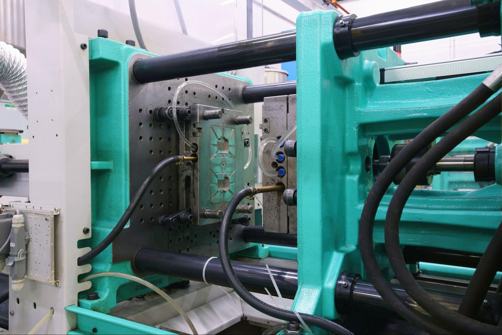 A teal colored injection molding press and steel mold.