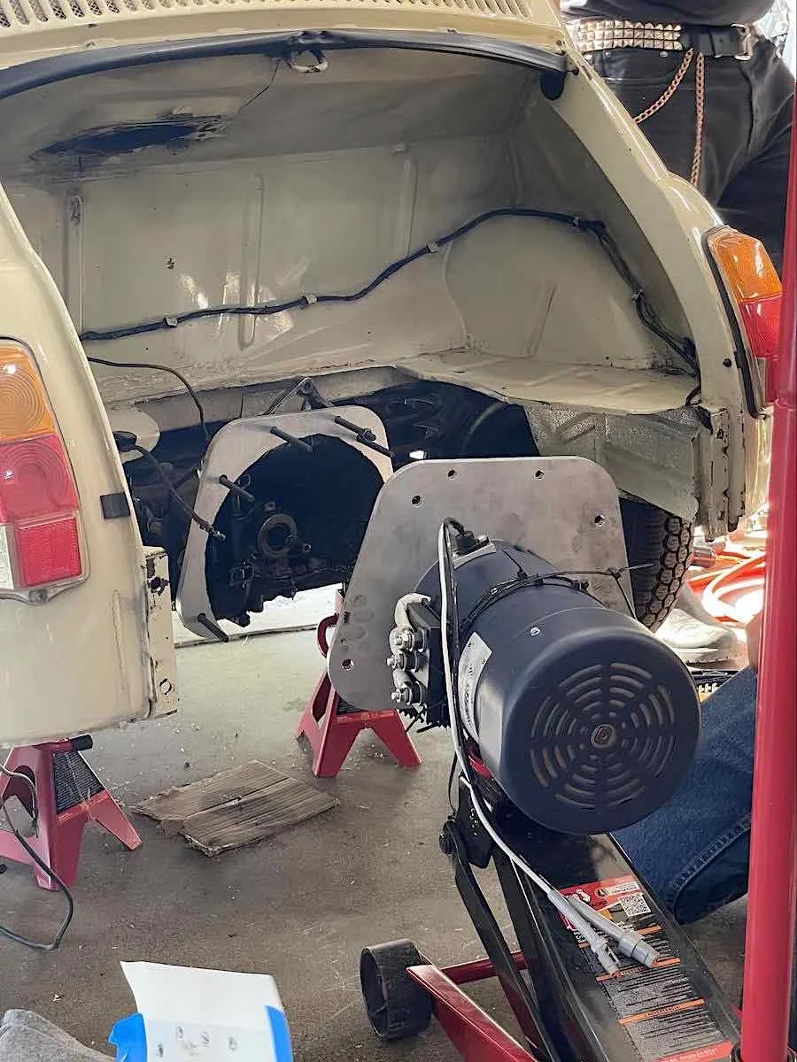 image of an electric motor with mounting plate attached supported by a floor jack being mounted to a fiat 500 driveshaft