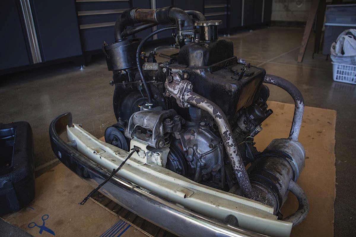 image of 1966 fiat 500 engine with bumper attached sitting on the floor of a garage