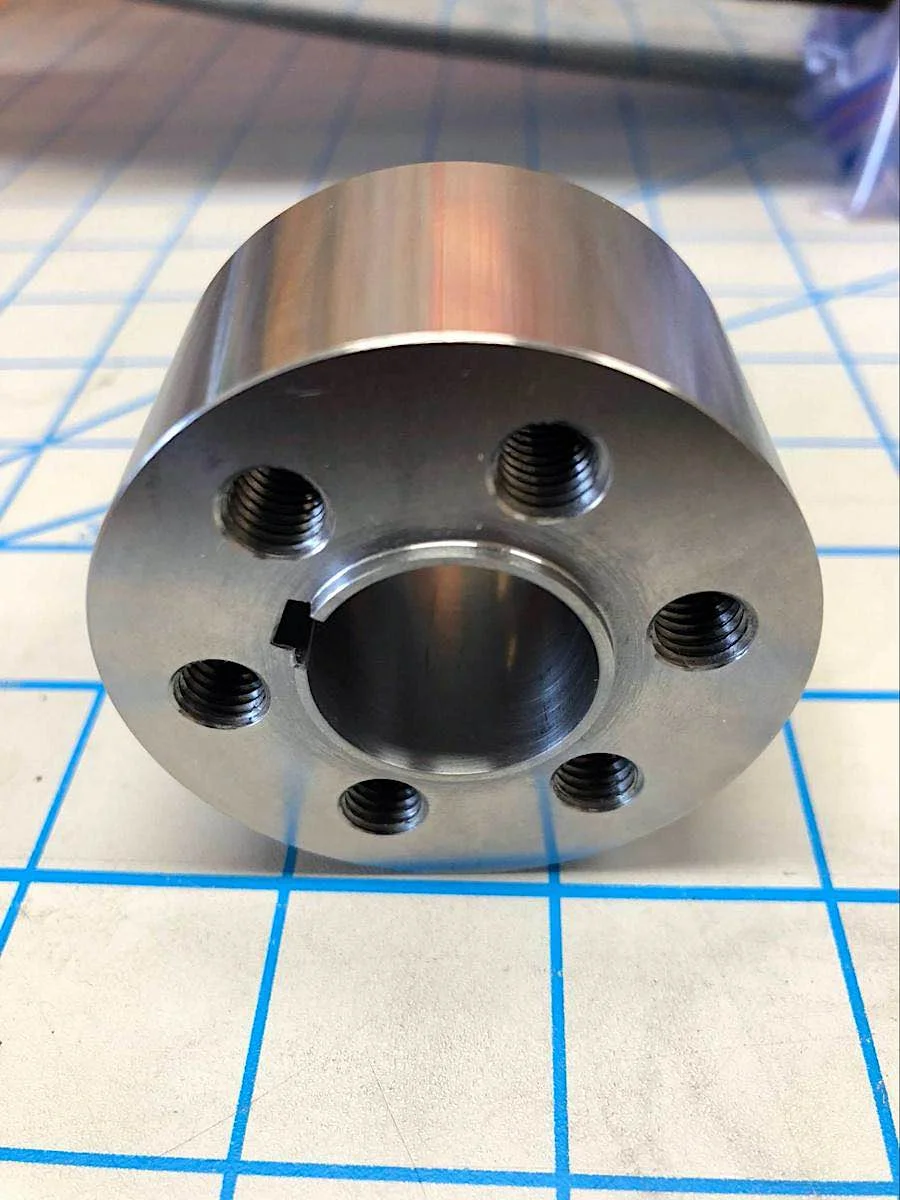image of a steel cnc machined drive shaft coupler from the bottom, showing six tapped holes surrounding a large hole in the middle