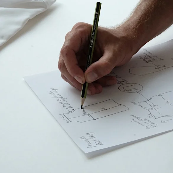 fictiv2image2 - Fictiv hand with a pencil drawing designs and dimensions on a white piece of paper on a white table