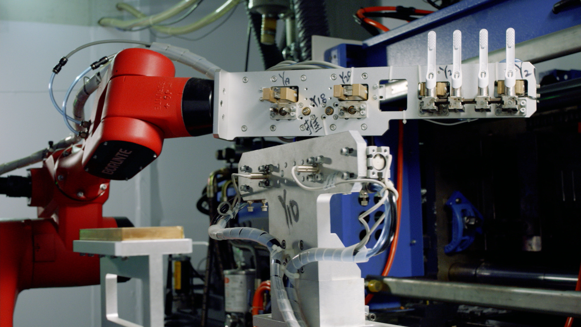 A robotic arm passes quip toothbrush heads between two injection molding machines for a two-shot production process.