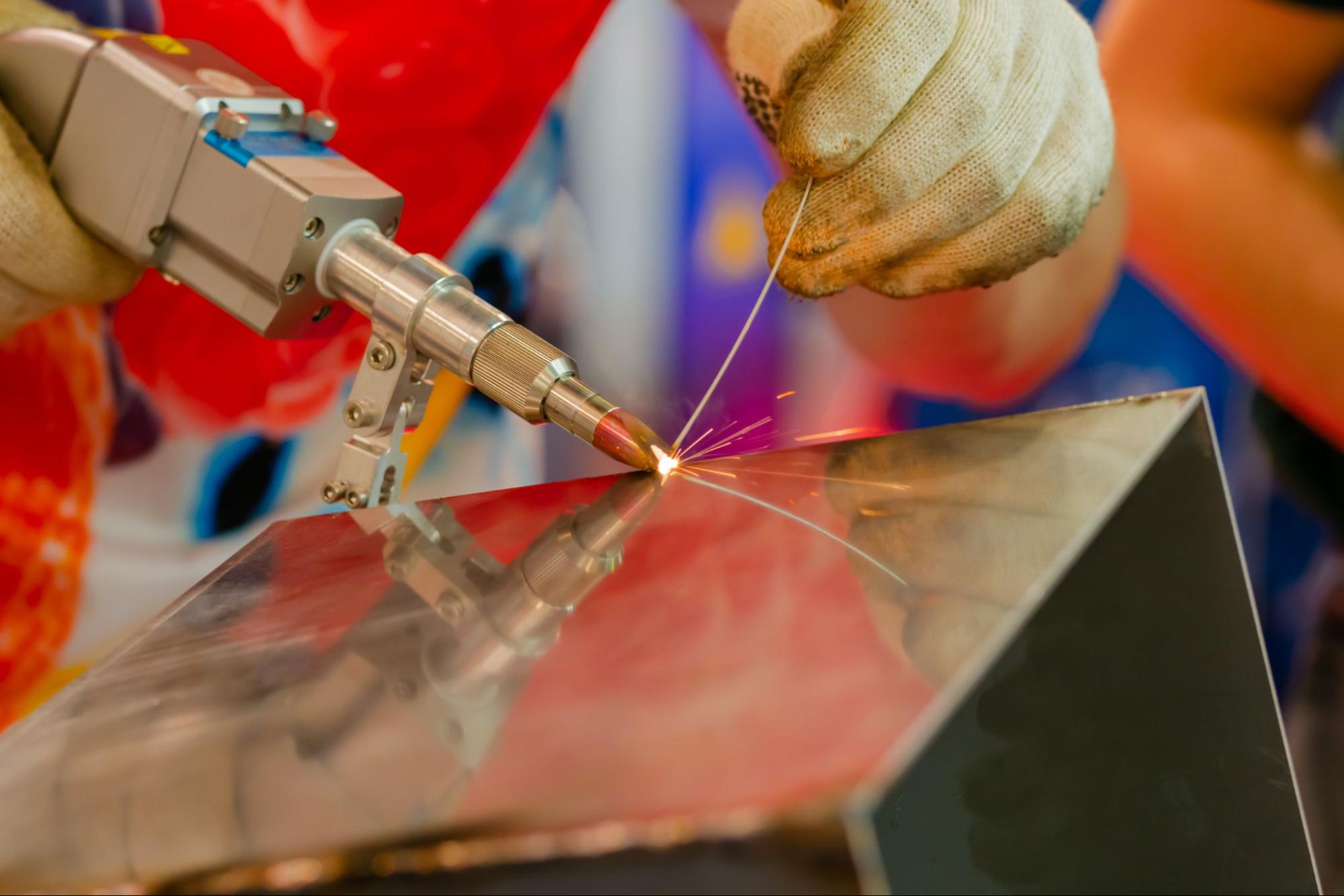 A worker laser welding the corner of a sheet metal box.