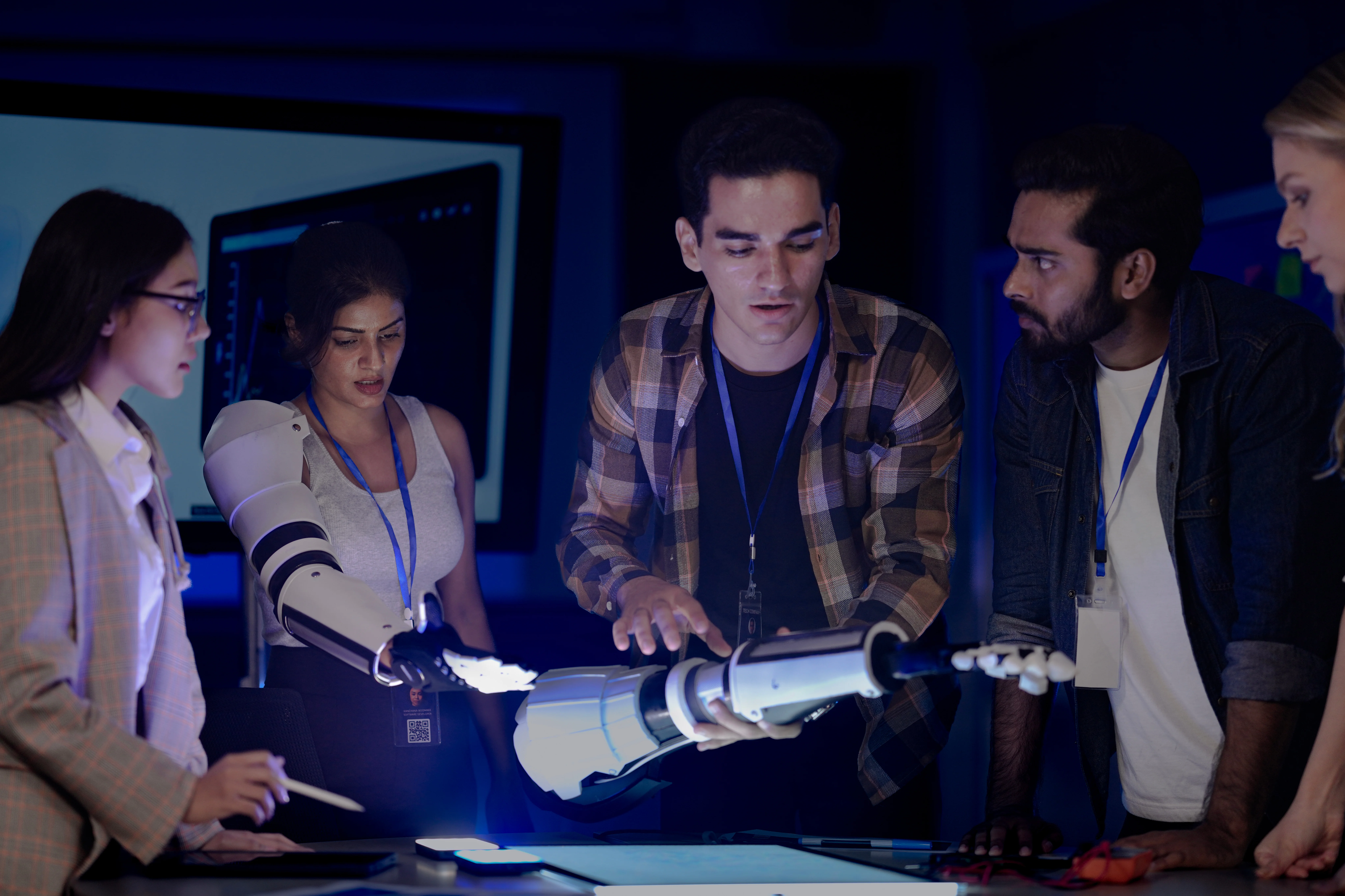 Robotics engineers in an RD lab test an AI powered prosthetic arm The diverse team including an Indian woman analyzes the bionic prototypes hardware and design at night - Fictiv engineering team evaluating robotic arm prototype