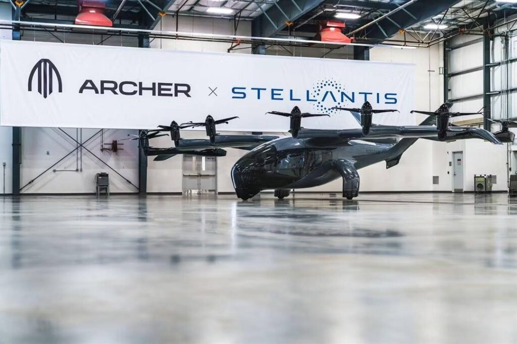 Sleek multi‑propeller aircraft in a hangar beneath a banner reading 'ARCHER × STELLANTIS'.