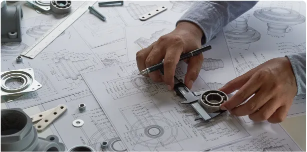 Hands using a caliper to measure a bearing on technical drawings and mechanical parts on a blueprint setup.