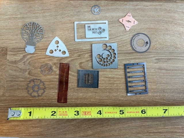 thin-metal-parts-feature - Fictiv Assorted small metal machine parts laid out on a wooden table, with a measuring tape at the bottom for scale.