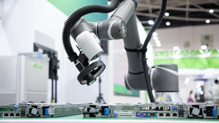 Industrial robotic arm with a gripper hovering over server blades on a lab bench.