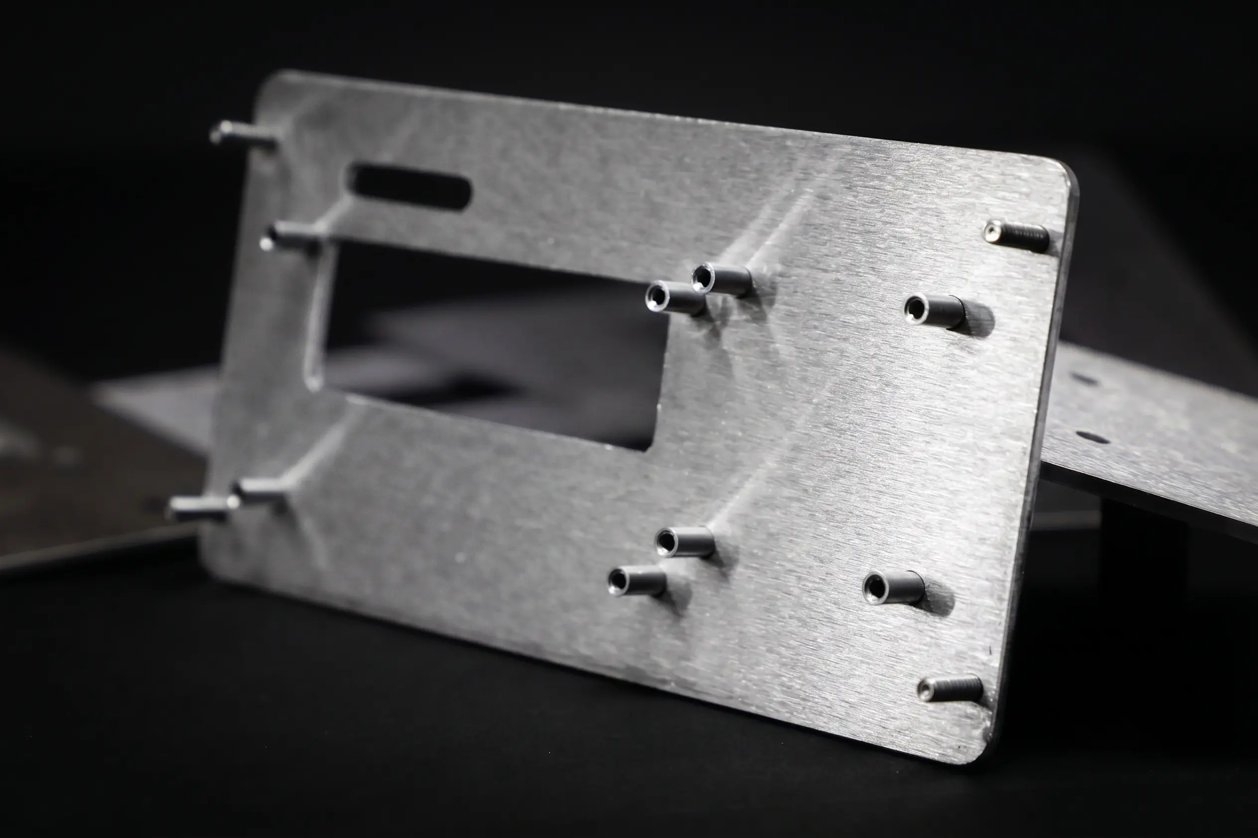 Brushed metal industrial bracket with multiple small cylindrical pins protruding from a plate against a dark background