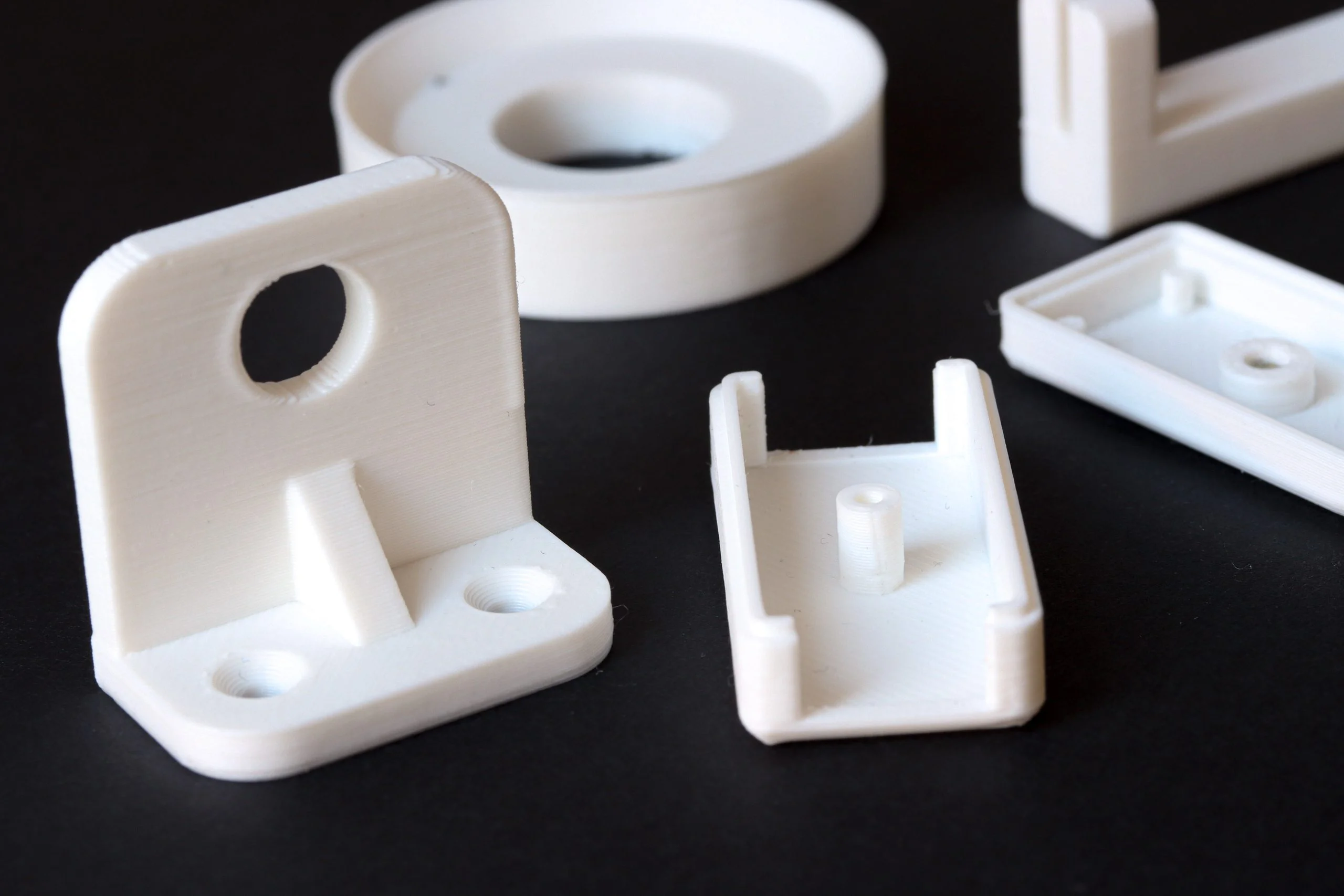 White PLA 3D printed prototype parts on black background - Fictiv FDM 3D printing creates anisotropic parts